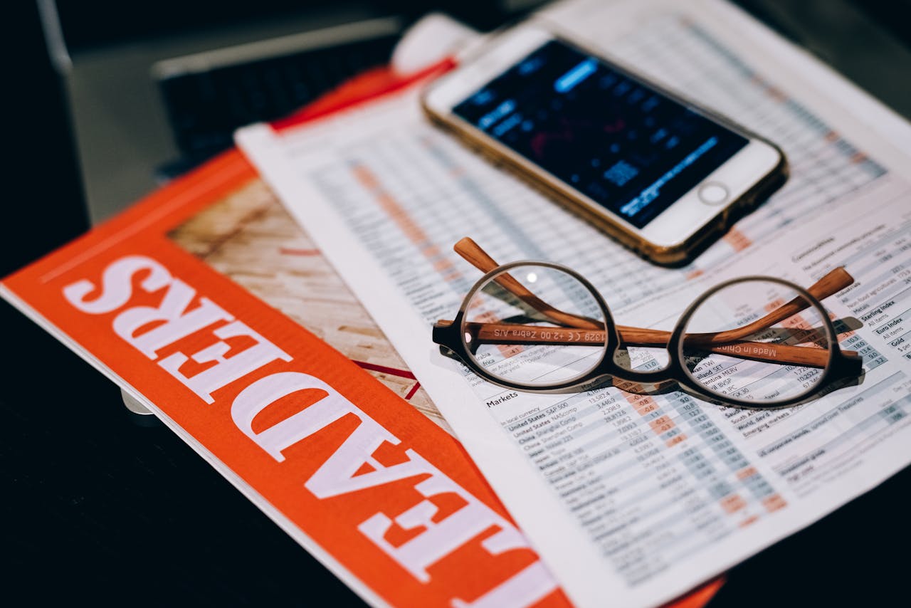 why-choose-us A close-up of business analytics tools including a smartphone, eyeglasses, and papers.